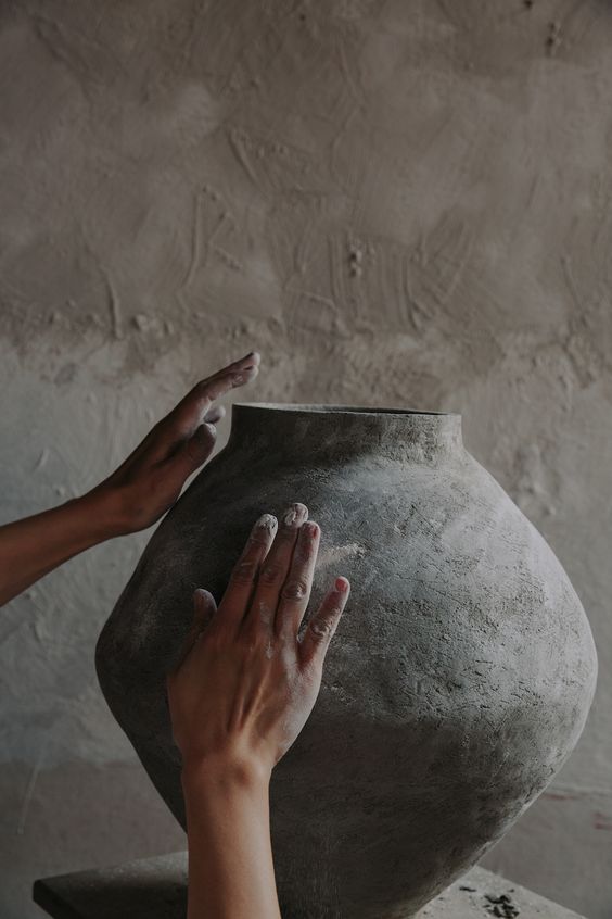 The Clay — Hands smoothing a large dark unfired pot